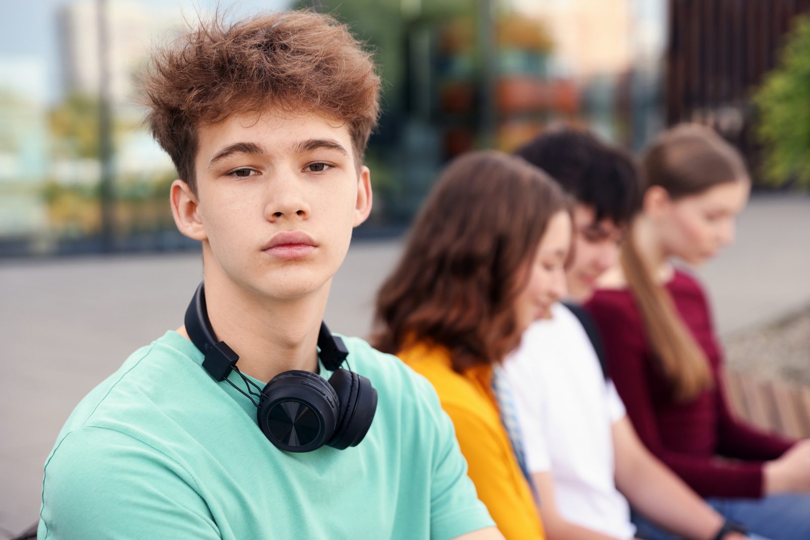 Teenage boy with headphones around his neck sitting with friends outside school